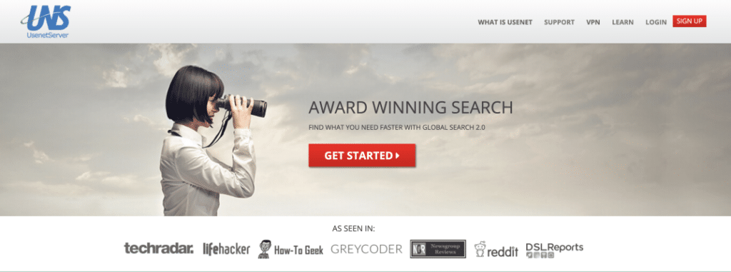 A woman with short, black hair is standing in front of a grey sky, She is looking at something off the right side of the screen with binoculars.