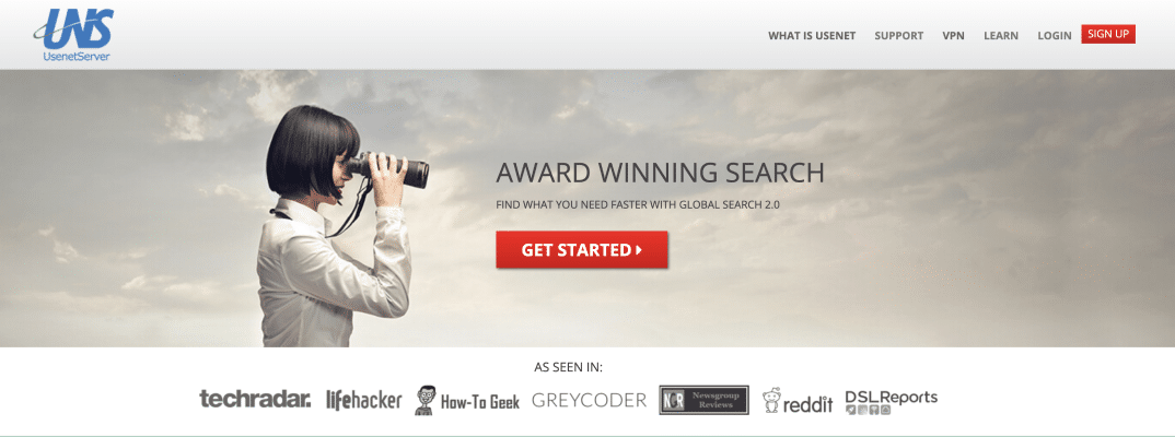 A woman with short, black hair is standing in front of a grey sky, She is looking at something off the right side of the screen with binoculars.