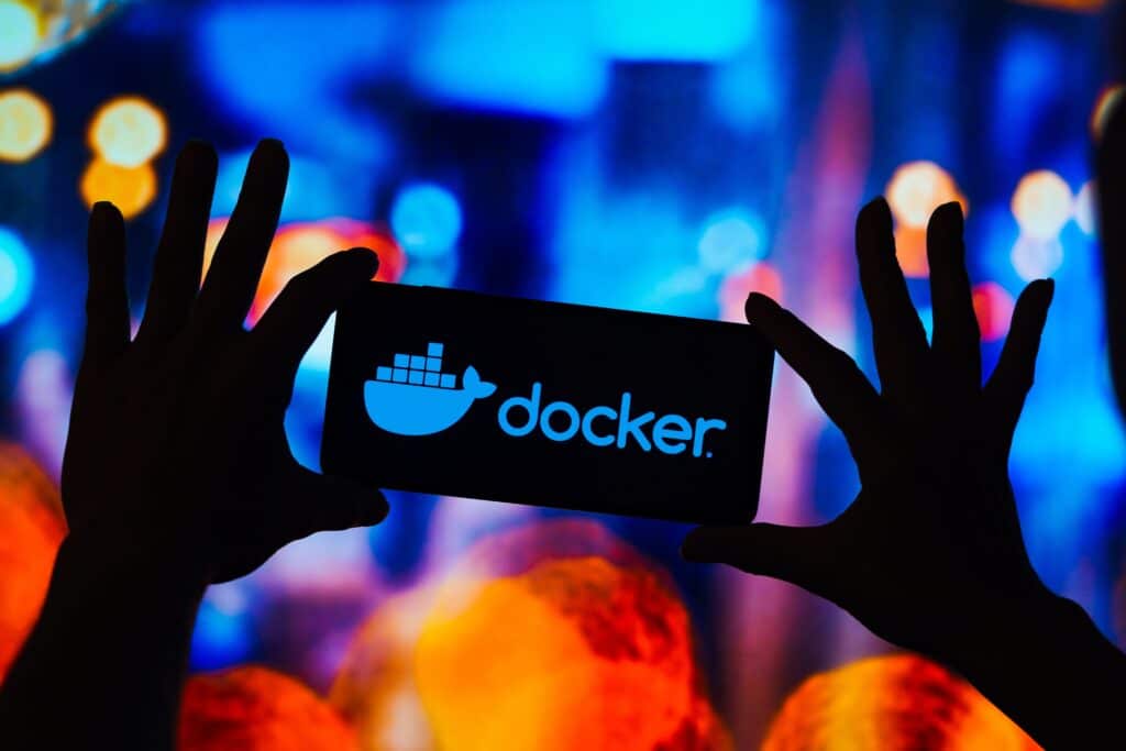 Two hands in silhouette holding a placard that shows the Docker logo and name as if light from behind it is passing through.