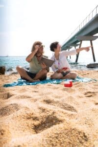 A couple is on the beach, pointing at something and holding a tablet.