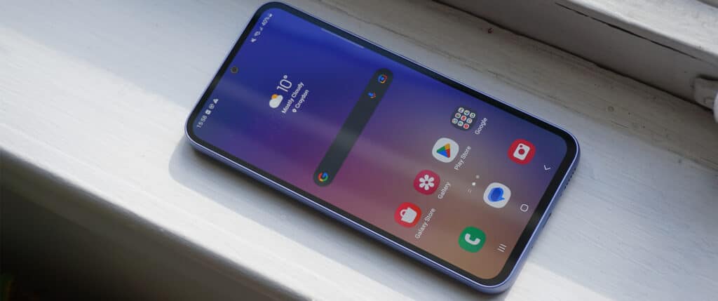 A Samsung Galaxy a54 with the home screen open sitting on a counter or windowsill.