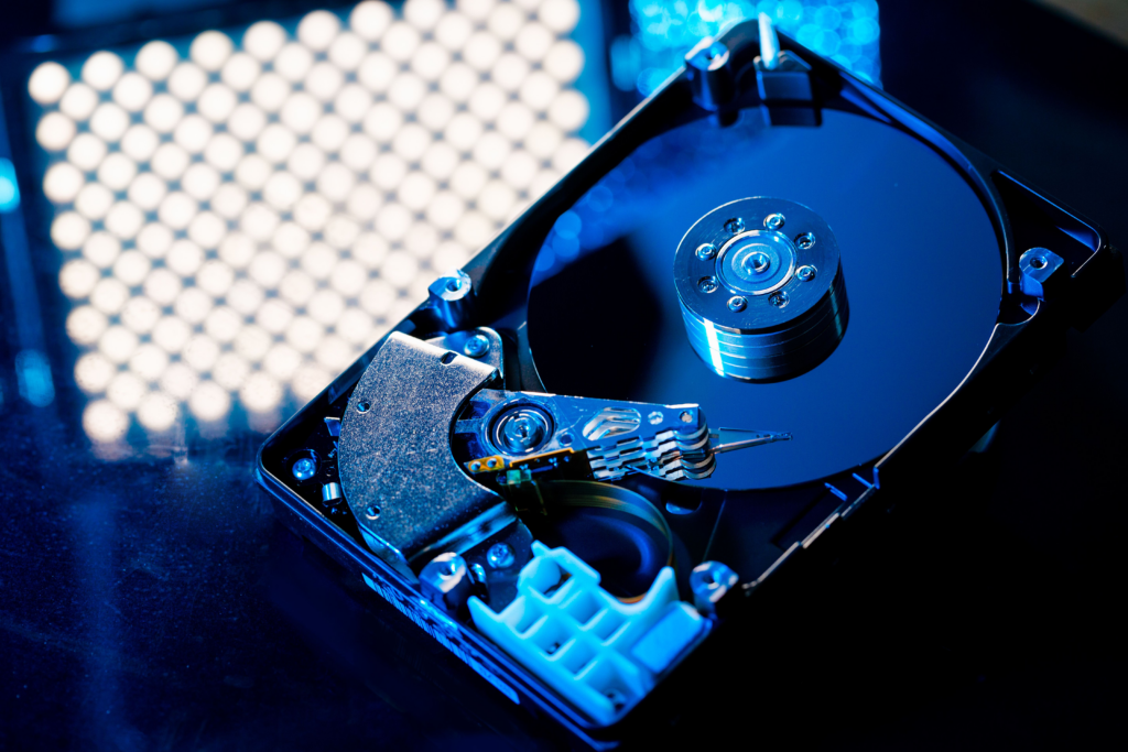 Closeup of a hard disk drive on a black glass table reflecting the lights above it.